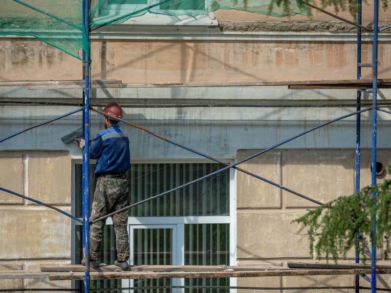 Operario enfoscando una fachada desde el andamio