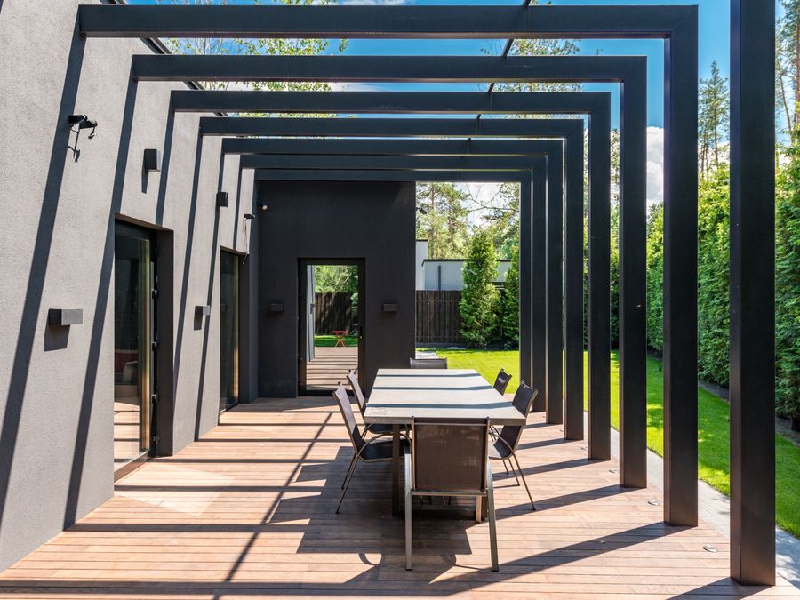 Porche cubierto sobre una terraza de madera, con mesa de comedor y jardín al fondo